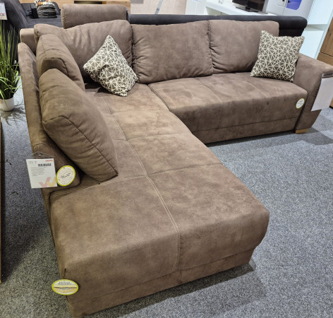 Wohnlandschaft „Larissa“, braunes L-förmiges Sofa mit Kissen und Gästebett, abgebildet auf einem grauen Teppich im Ausstellungsraum.