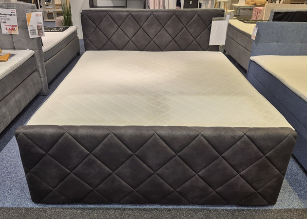 Boxspringbett „Corby“ in Anthrazit in Lederoptik, mit rautenförmigem Kopfteil und praktischen Bettkästen.