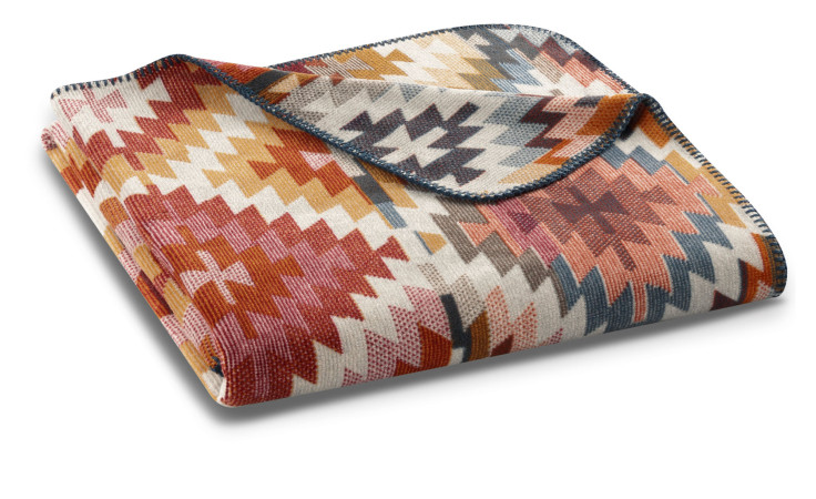 Eine gefaltete Biederlack Wohndecke Nomad Light 150x200 cm mit Zickzack-Muster in rot, orange, gelb, navy & beige.