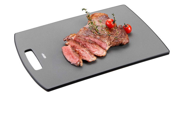 In Scheiben geschnittenes Steak mit Kräutern und Tomaten auf dem schwarzen GEFU Schneidebrett Levoro, auf weißem Hintergrund.