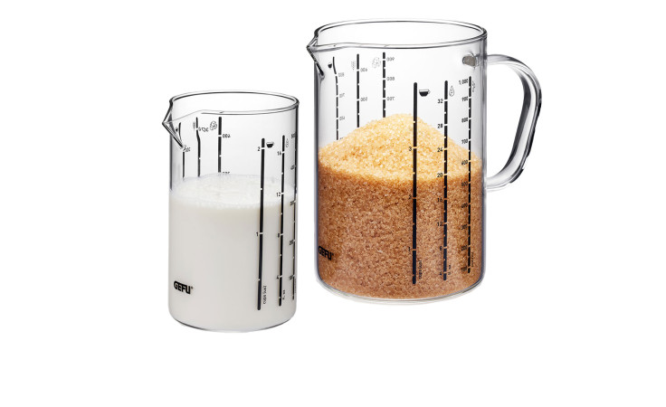 Zwei GEFU Meti Messbecher - einer mit Milch, einer mit braunem Zucker - stehen auf einem weißen Hintergrund.
