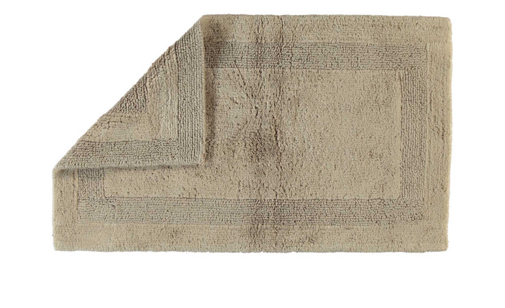 Ein beiger Cawö Wende-Badeteppich 60x100 cm, dessen Ecken gefaltet sind, um das strukturierte Randmuster zu enthüllen.