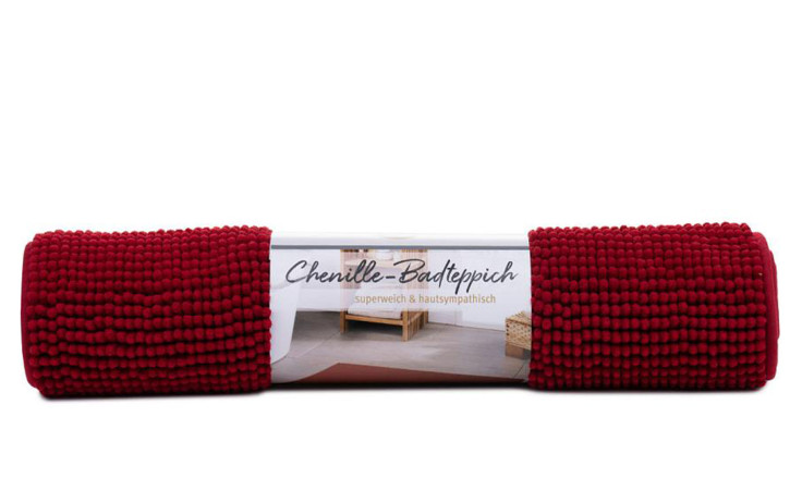 Ein aufgerollter Gözze Badteppich Chenille 60 x 100 cm mit strukturierter Oberfläche und Etikett, Bordeaux.