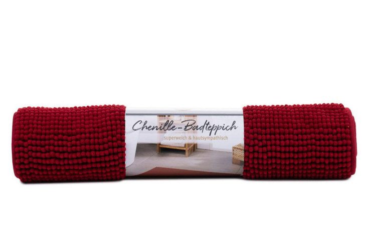 Ein aufgerollter Gözze Badteppich Chenille 70 x 120 cm mit deutschem Etikett, vor einer Badezimmerszene.