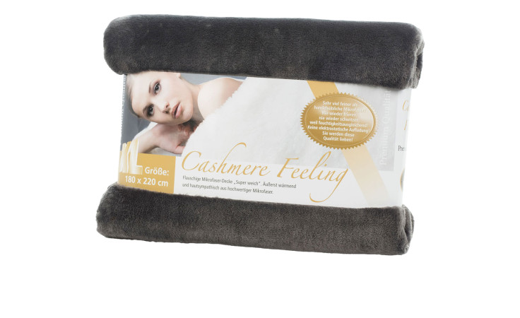 Gözze Wohndecke Premium Cashmere Feeling 180x220cm in einer Verpackung mit einem Foto einer Frau, die in eine weiche weiße Decke gehüllt ist.