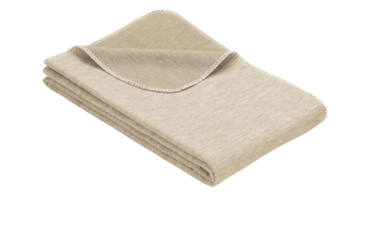 Eine gefaltete beigefarbene Baumwolldecke 140 x 200 cm mit genähten Rändern auf weißem Hintergrund.