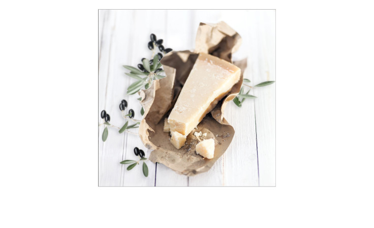 Ein Stück Hartkäse mit Olivenzweigen auf braunem Papier, abgebildet auf Pro-Art Glasbild Mediterrean Food 20x20 cm.