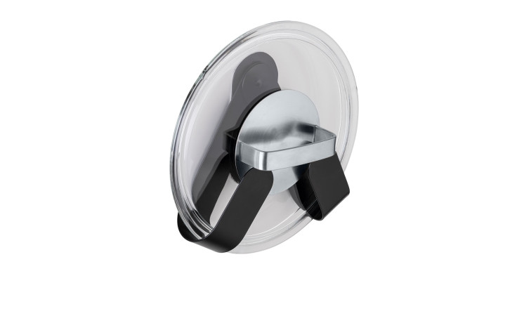 Ein gläserner Topfdeckel wird von dem an der Wand befestigten, schwarz-silbernen Topfdeckelhalter Tony aufrecht gehalten.