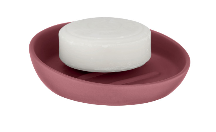 Ein rundes weißes Seifenstück liegt in einer Seifenablage Badi, einer rosafarbenen Seifenschale mit einem geschlitzten Boden.