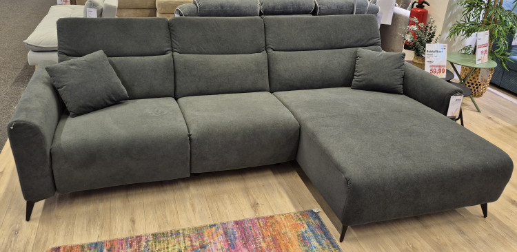 Wohnlandschaft „Triest“ in Dunkelgrau mit schwarzen Metallbeinen, abgebildet auf einem Holzboden neben einem bunten Teppich.