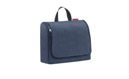 Die Reisenthel Kulturtasche Toiletbag XL in dunkelblauem Fischgrätmuster steht aufrecht mit einem Henkel auf weißem Grund.