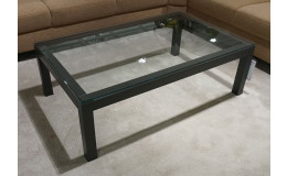 Couchtisch „Vilano Skara“ mit Glasplatte, graphitschwarzem Gestell, auf hellem Teppich, umgeben von braunen Sofas.