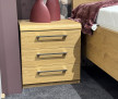 Wildeiche-Nachttisch mit 3 Schubladen, Metallgriffe; neben dem Bett „MONDO Comfort Plus“, lila Decke.