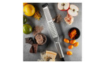 GEFU Fein- und Grobreibe Primeline mit Äpfeln, Zitrusfrüchten, Kumquats, Käse, Gewürzen und Schalen auf einer grauen Oberfläche.