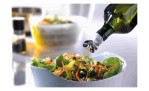 GEFU Ausgießer Automatico gießt Olivenöl über Salat und Möhren in einer weißen Schüssel.