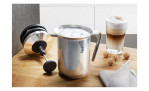 Der GEFU Milchaufschäumer Riccardo schäumt Milch für Milchkaffee und Snacks auf, dargestellt auf einer Holzfläche.