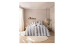 Ein gemütliches Schlafzimmer mit Estella Mako-Jersey-Bettwäsche Tavaro 155x220, einem runden Teppich, Pflanzen und Licht durch transparente Vorhänge.