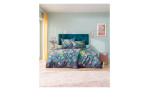 Ein Bett mit Mako-Satin-Bettwäsche Bonny, tealfarbenem Kopfteil und farbenfrohen Kissen in einem Schlafzimmer mit Pastelltönen.