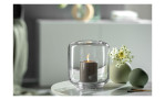 Eine brennende Kerze in einem Glashalter sitzt neben zwei Leonardo Vase Bolla 7 cm mit weißen Blumen.