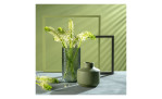 Grüne Blumen in einer 29 cm großen Leonardo-Vase Martello und einer mattgrünen Keramikvase auf einer Oberfläche in Grau mit geometrischen Rahmen.