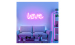 Ein LED-Bild - Neon-Love-Schild leuchtet neonpink über einem grauen Sofa mit Pflanzen und Dekoration in einem modernen Wohnzimmerregal.