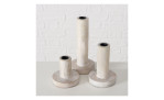 Drei Kerzenleuchter Pekat 22 cm in Holzfarbe stehen auf einer weißen Fläche vor einer weißen Backsteinwand.