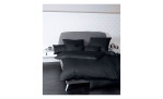 Mako-Satin Kissenbezug Colors, in der Größe 80 x 80 cm und in der Farbausführung schwarz, auf einem Bett bezogen mit der passenden Bettwäsche und weiteren Kissen