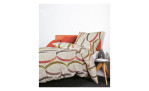 Ein Bett mit Biber Bettwäsche 155x220 cm Taupe Siena, ein orangefarbener Kopfkissenbezug und ein Nachttisch mit Büchern und Dekoration.