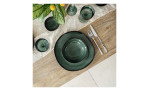 Der Speiseteller Lave vert von Villeroy & Boch, 28 cm, auf Holztisch mit Besteck, Gläsern, Läufer und Pflanze.