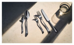 Ein WMF Besteck-Set Sitello 30-tlg. und ein Glas Wasser auf einer hellen Fläche mit dramatischen Schatten.