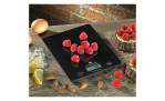 Die Digitale Küchenwaage Balance aus schwarzem Kunststoff mit Glas-Oberfläche, gezeigt mit Himbeeren, Eiern und Gebäck.