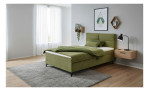 Olivgrünes Boxspringbett Carmen mit passenden Kissen und einem freistehenden Nachttisch mit Lampe.