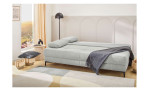 Das Schlafsofa „Faye“ in Hellgrau mit Kissen, einer dunklen Decke und der idealen Höhe für ein modernes, sonniges Wohnzimmer.