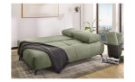 Das Schlafsofa „Giulia“ in Hellgrün mit Kissen, einer schwarzen Decke und einem Korb in einem hellen Raum mit Meerblick.