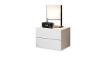 Nachttisch Carry in weiß mit zwei Schubkästen schräg links von der Seite abgebildet. Dekoriert mit einer Lampe und einem Wecker.