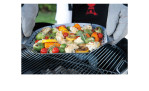 Handschuhe halten einen Weber Gemüsekorb Groß über einen Gasgrill, bereit zum Grillen im Freien.