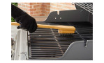 Eine behandschuhte Hand benutzt die Weber Grillbürste Bambus, 45 cm, um den Grillrost auf einem Außengrill zu reinigen.