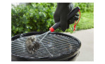 Eine behandschuhte Hand reinigt einen Grillrost mit der Weber Grillbürste dreiseitig, 30 cm, im Freien.