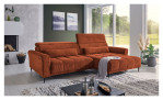 Wohnlandschaft Lilly in Orange mit Kopfteilverstellung und Ottomane rechts, inszeniert auf gemustertem Teppich vor einer großen Fensterfront.