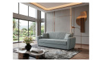 Modernes Wohnzimmer mit einem 3-Sitzer-Sofa „Aiden“, einem Glastisch, einer Stehlampe und Fenstern, die den Blick auf einen üppigen Garten freigeben.